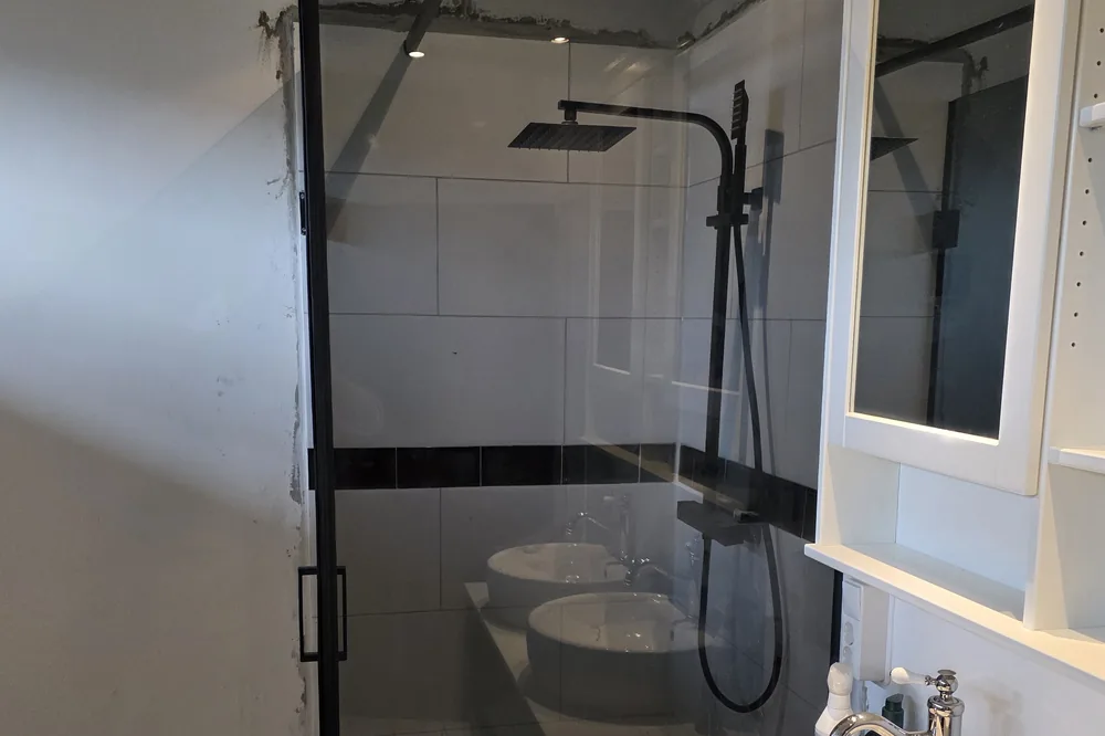 Afgewerkte badkamer met zwarte inloopdouche en wastafel.