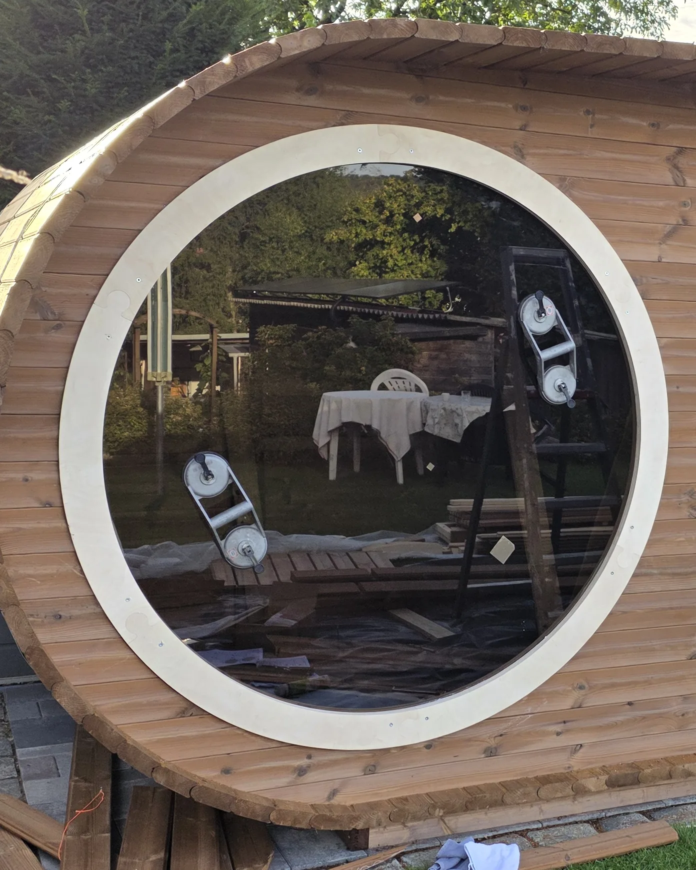 Handgebouwde buitensauna in cederhout met rond patrijspoortraam, in avondlicht.