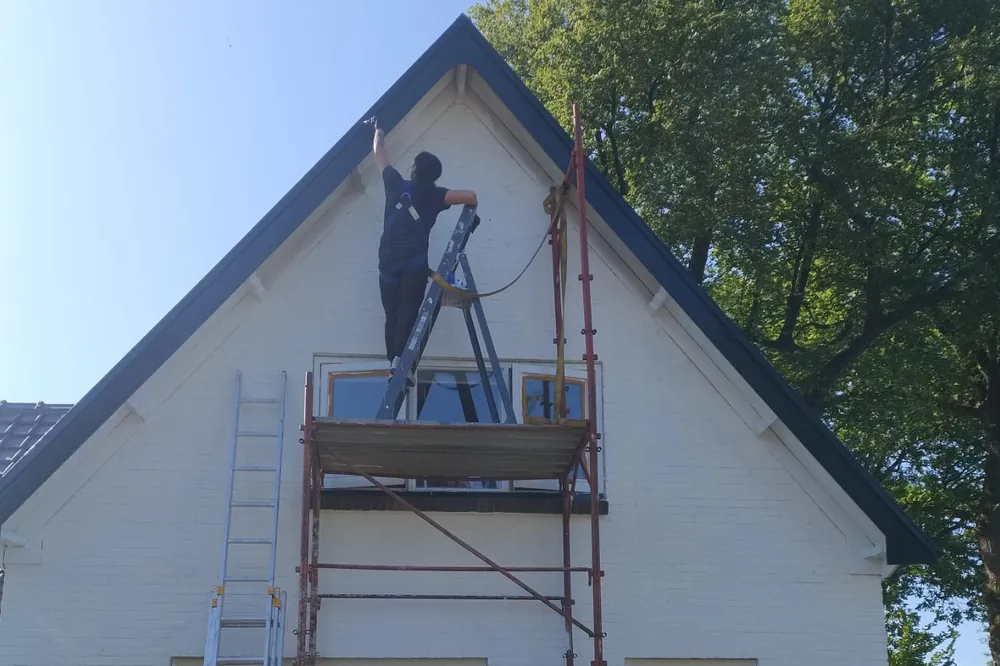 Diana schildert vanaf een ladder op de steiger de nok van een witte gevel.