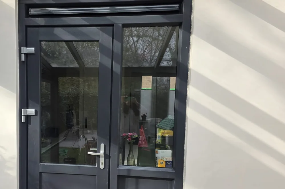 Serre met stalen kozijnen en glazen deuren, muren afgewerkt in een warme crèmetint.